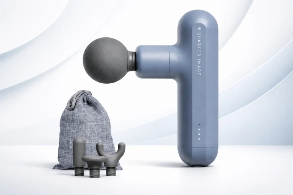 Sharper Image massage gun with attachments and carry pouch on a clean light gradient studio background