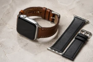 Brown leather Apple Watch band with stitched edges beside a black replacement strap